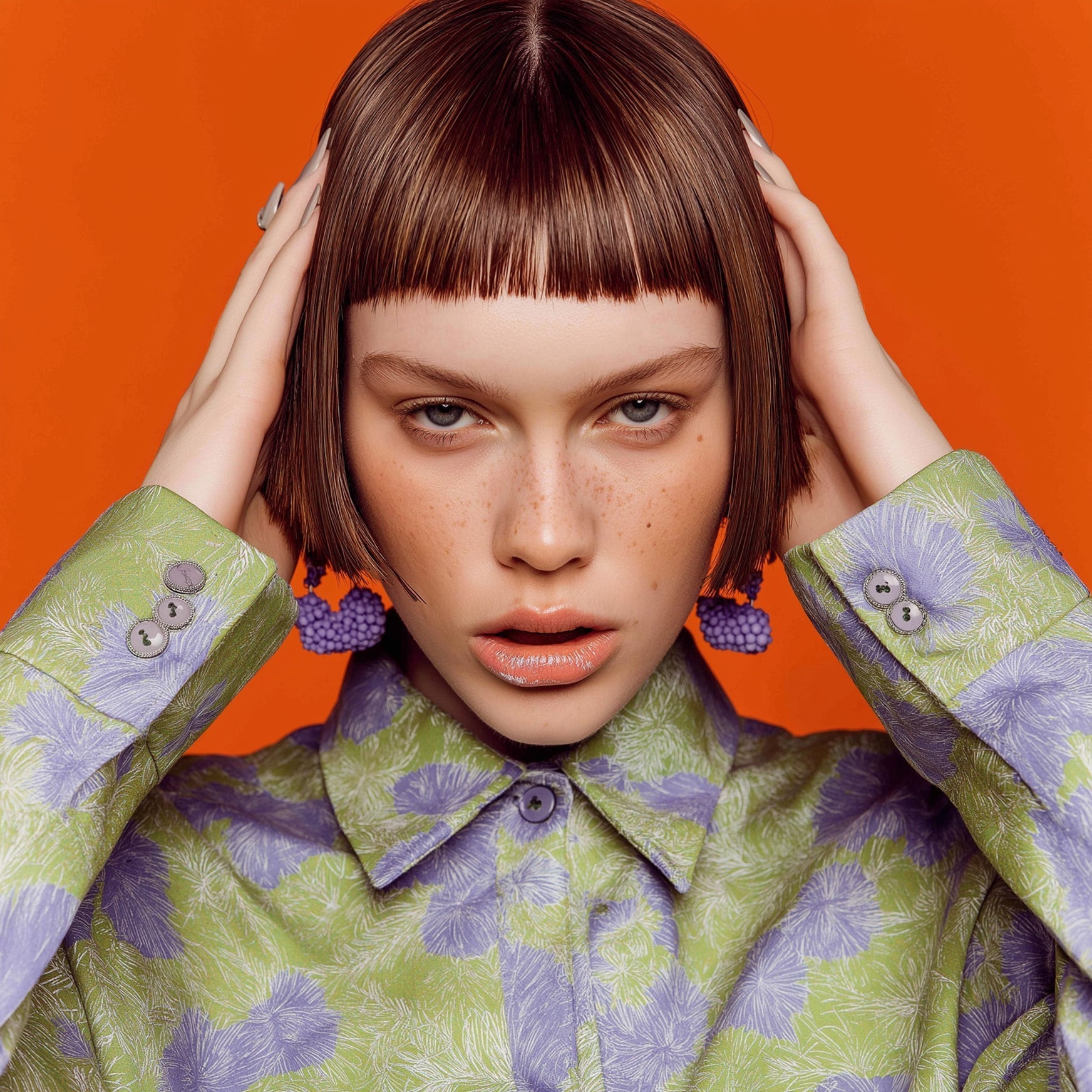 Fashion portrait of woman with short bob haircut wearing floral green and purple outfit against orange background