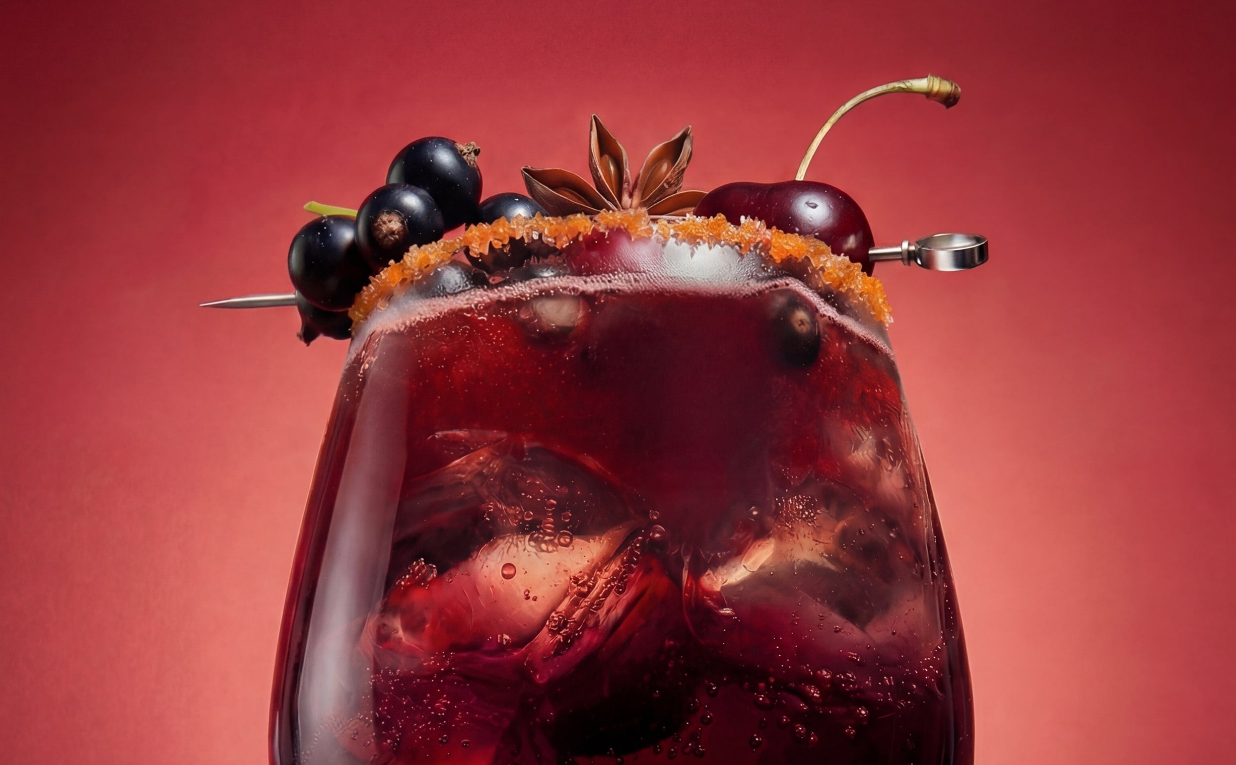 Dark berry cocktail with cherries, blackcurrants, ice cubes, and spiced rim garnish