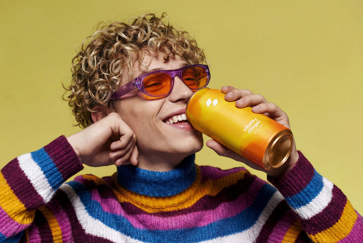 Person wearing colorful sunglasses and a striped sweater, drinking from a yellow cup against a yellow background
