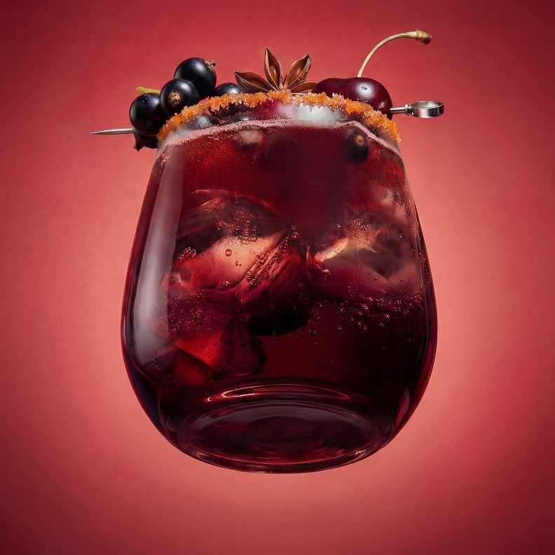 Red cocktail with cherries and berries on a red background