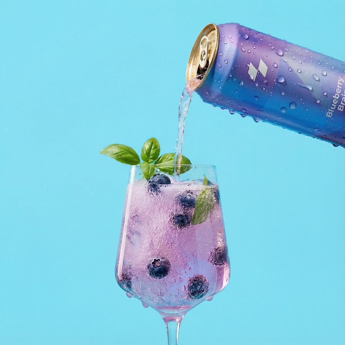 Blueberry-bramble drink being poured from a can into a glass with blueberries and mint leaves on a light blue background.