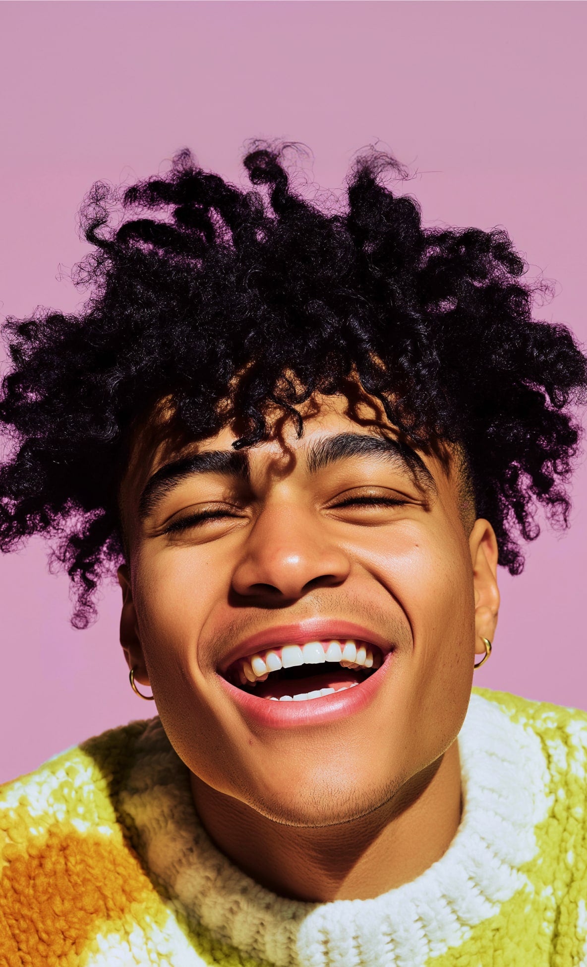 Person with curly hair wearing a colorful sweater against a pink background