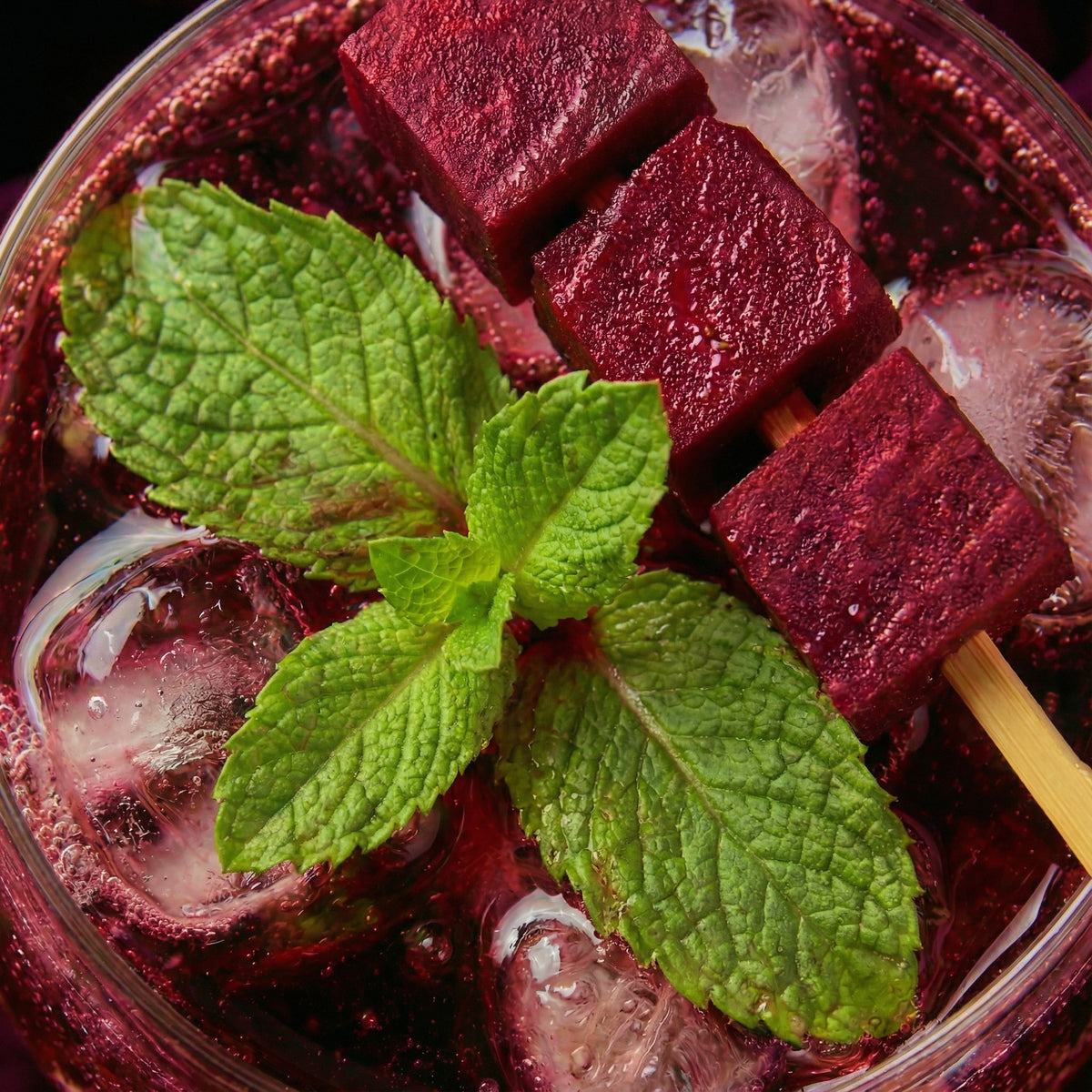 Close-up of a red drink with ice cubes, mint leaves, and a popsicle.