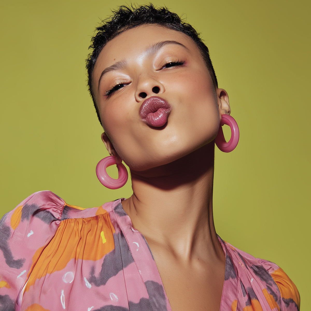 Woman wearing pink hoop earrings and a colorful top against a green background