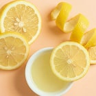 Lemon slices and a bowl of lemon juice on a peach background