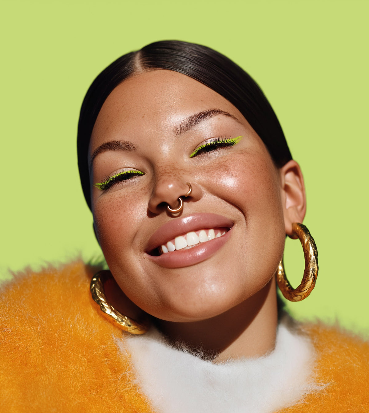 Woman with gold hoop earrings and green eyeshadow against a green background