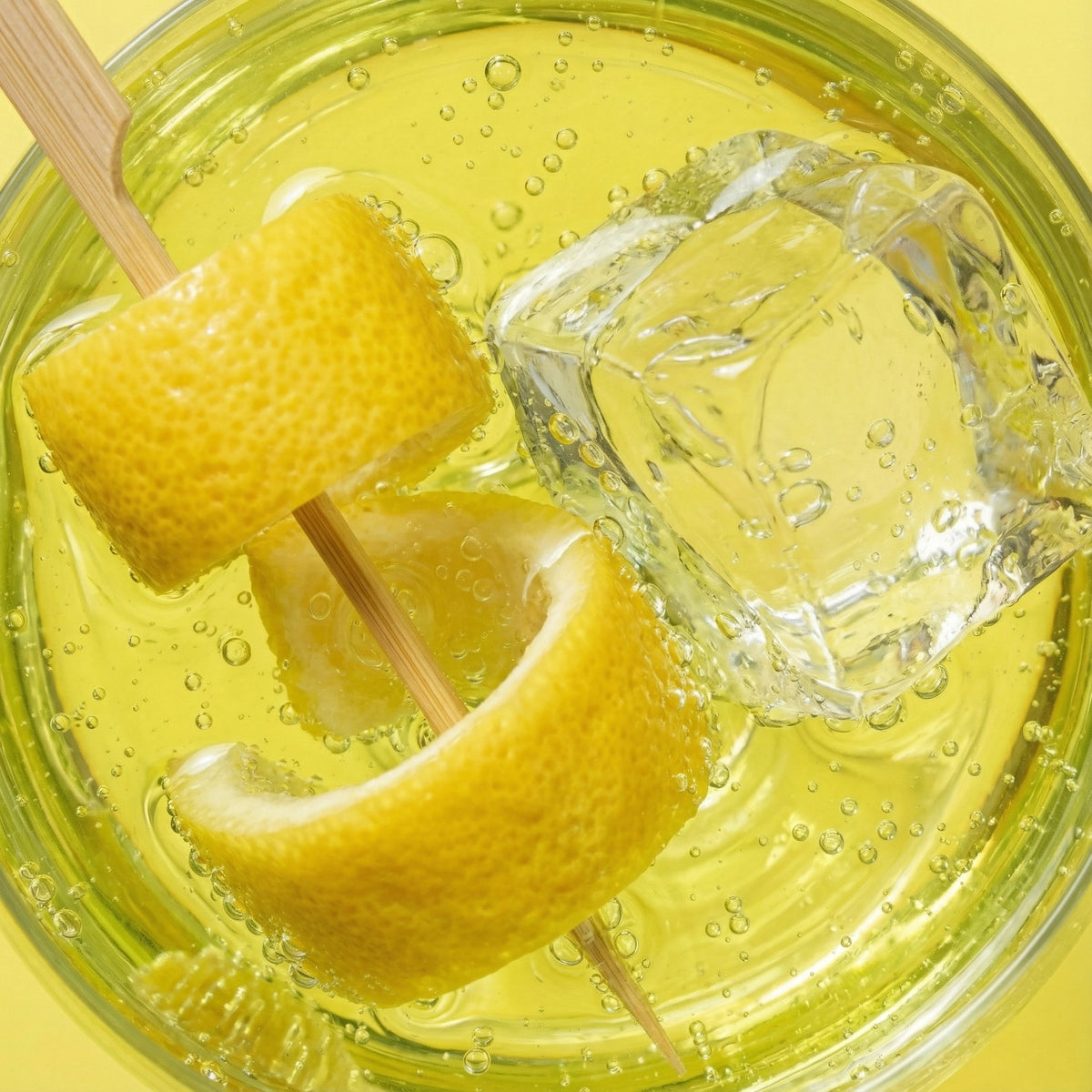 Glass of lemonade with lemon wedges and ice cubes on a yellow background
