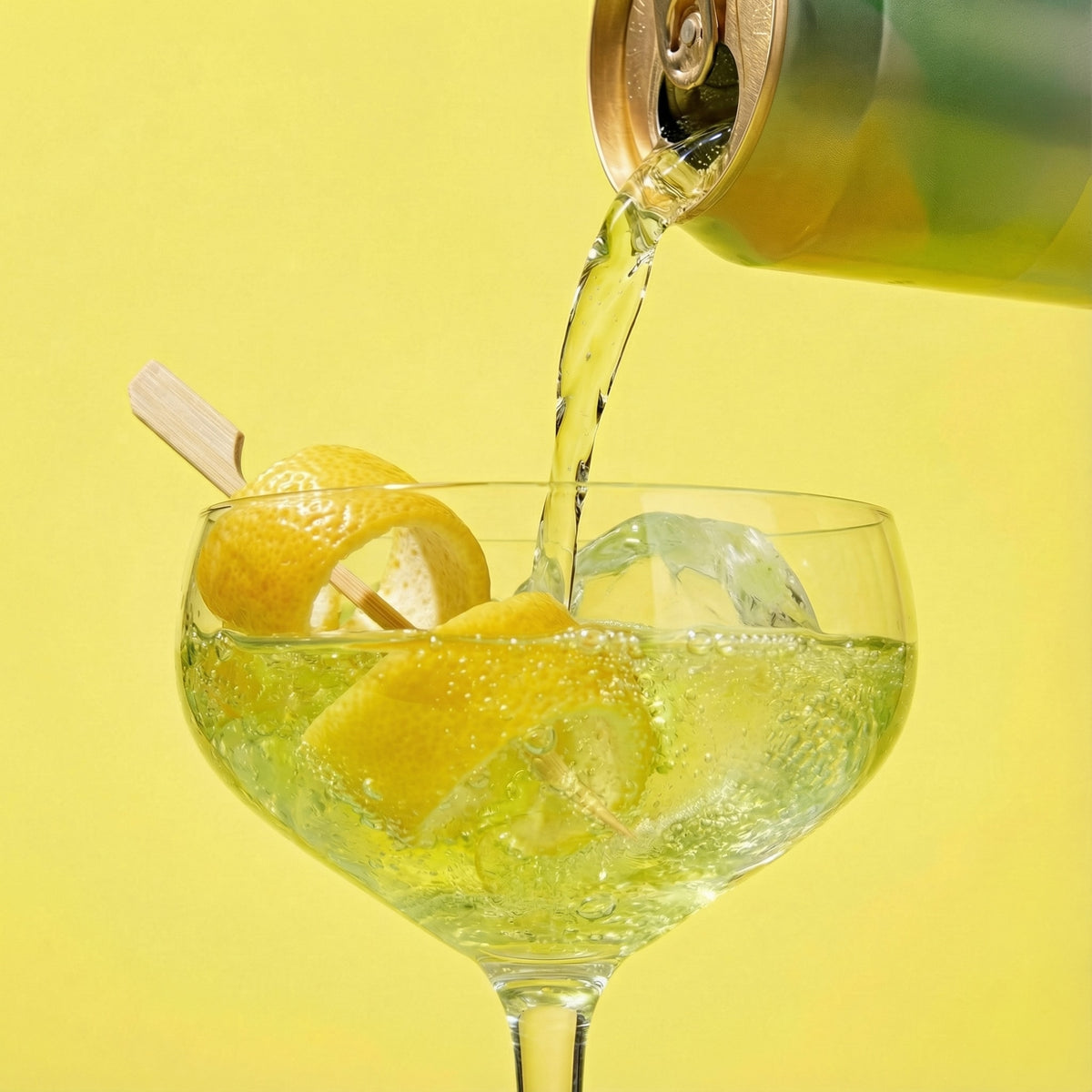 Alcohol being poured into a glass with lemons and ice on a yellow background