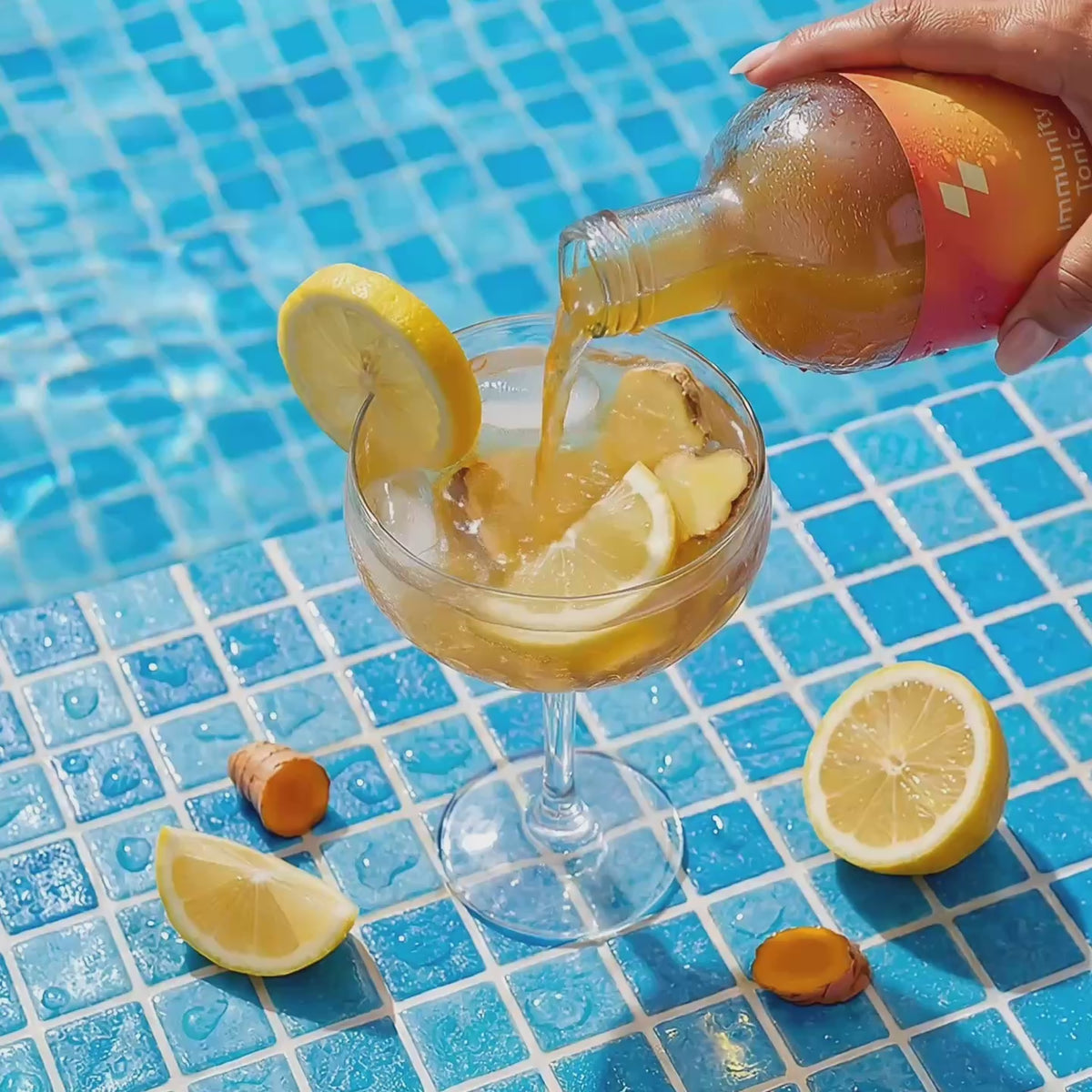 Pouring citrus cocktail by the pool with lemon and ginger slices