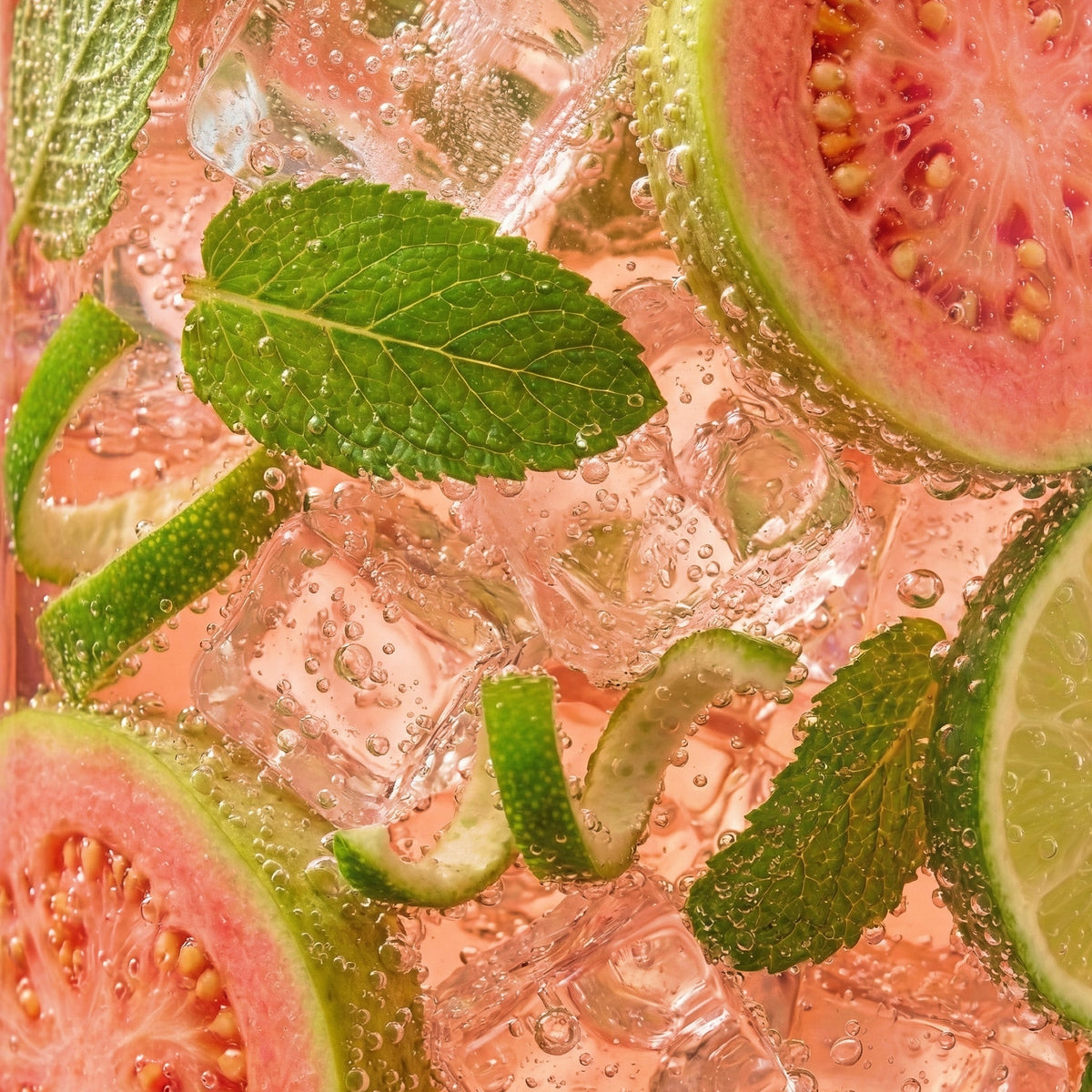 Sliced guava, lime, and mint leaves in a pink drink with ice cubes.
